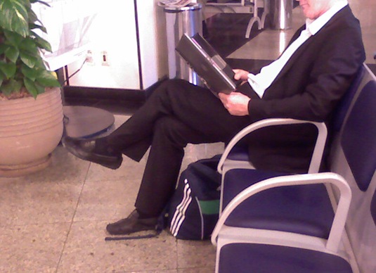 Homem no aeroporto segurando um notebook como se fosse um caderno